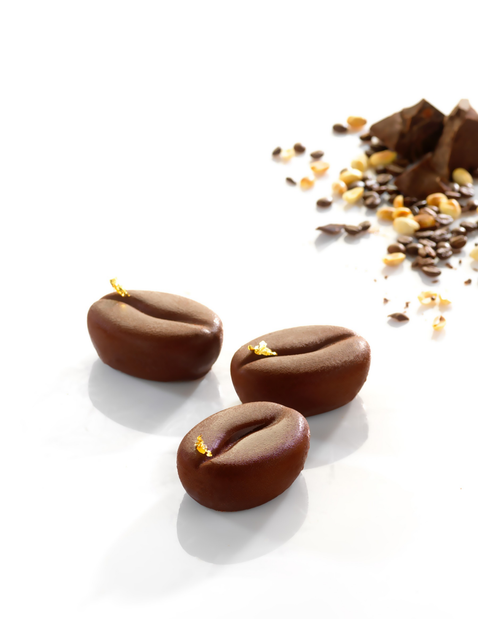 chocolats-artisanaux-grains-cafe Trois chocolats artisanaux en forme de grains de café, décorés de feuilles d'or sur un fond blanc.