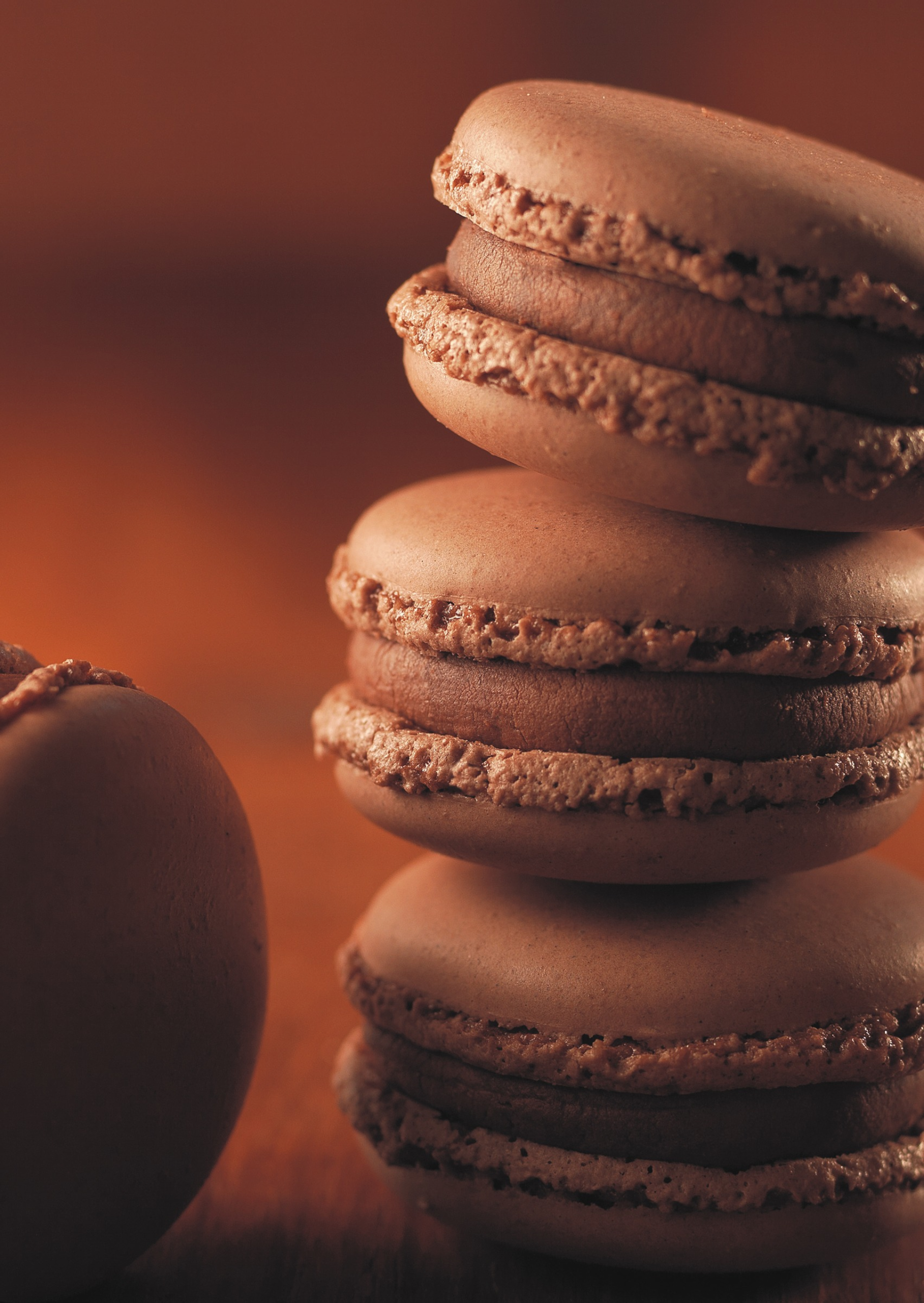 photographe-culinaire-macarons-chocolat-alsace Gros plan de macarons au chocolat empilés, photographiés avec une lumière chaude mettant en valeur leurs textures et leur garniture.
